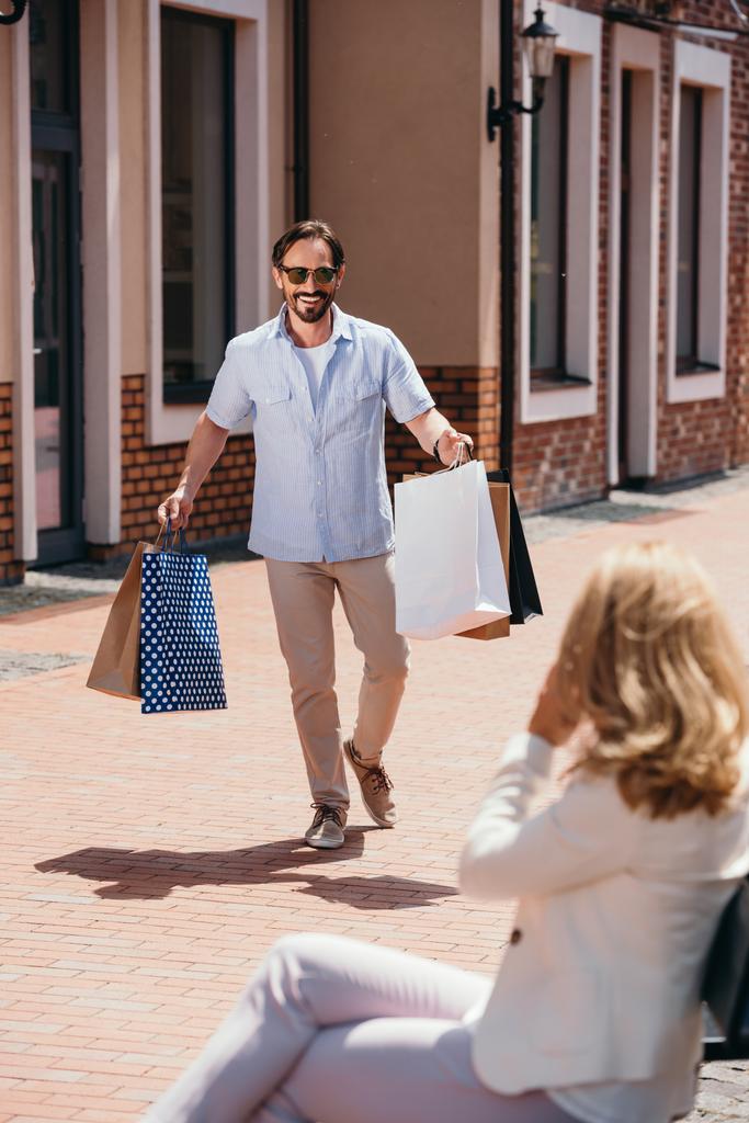 mulher sentada no banco e homem andando com sacos de compras
 - Foto, Imagem