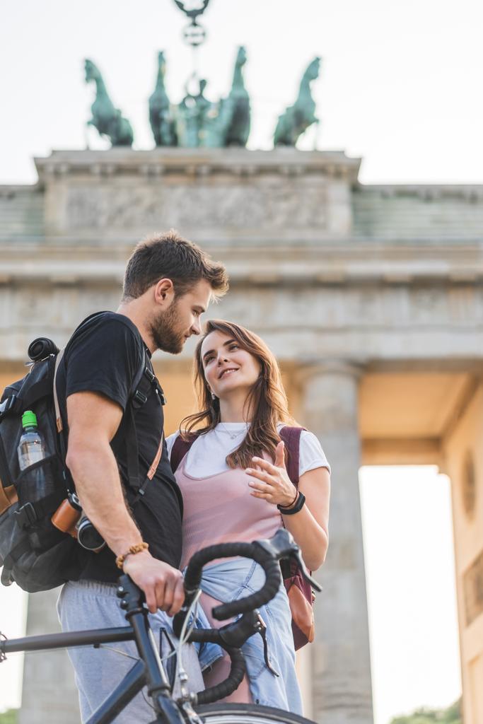 low angle view of woman talking to boyfriend with bicycle in front of Brandenburg Gate in Berlin, Germany  - Photo, Image