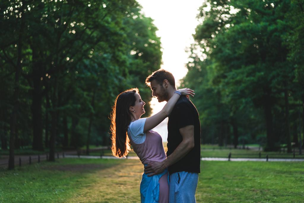 公園の草原で抱き合ってカップルを笑顔の側面図  - 写真・画像