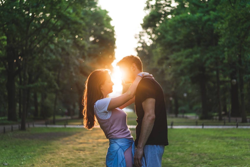 vista lateral de la mujer sonriente abrazando novio durante la puesta del sol
 - Foto, Imagen