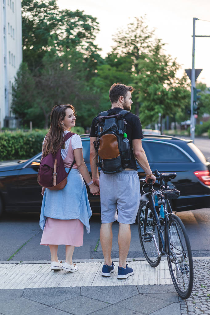 vue arrière du couple avec sacs à dos et vélo marchant dans la rue urbaine
  - Photo, image