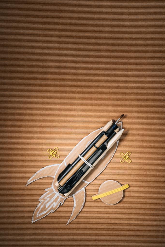 top view of handmade cardboard rocket with stationery and planet on brown background - Photo, Image