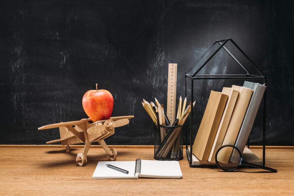 木製のおもちゃの飛行機、ノート、本、卓上を背後にある空の黒板の上に鉛筆でリンゴのビューをクローズ アップ - 写真・画像