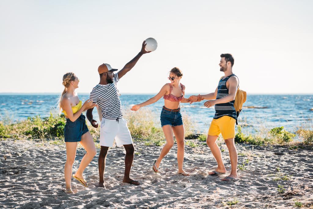 felizes jovens amigos multiétnicos brincando com bola na praia de areia
 - Foto, Imagem