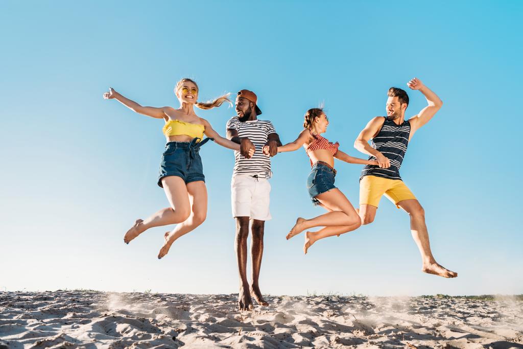 heureux jeunes amis multiethniques tenant la main et sautant dans la plage de sable
 - Photo, image