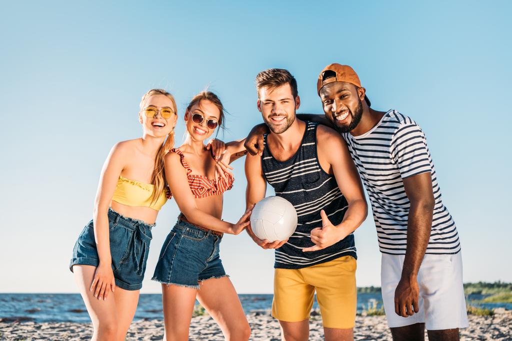 щасливі молоді багатоетнічні друзі з м'ячем, посміхаючись на камеру на пляжі
  - Фото, зображення