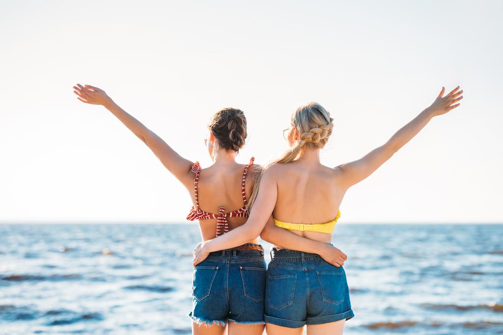 vue arrière de jeunes copines embrassant et levant les mains tout en regardant la mer
 - Photo, image