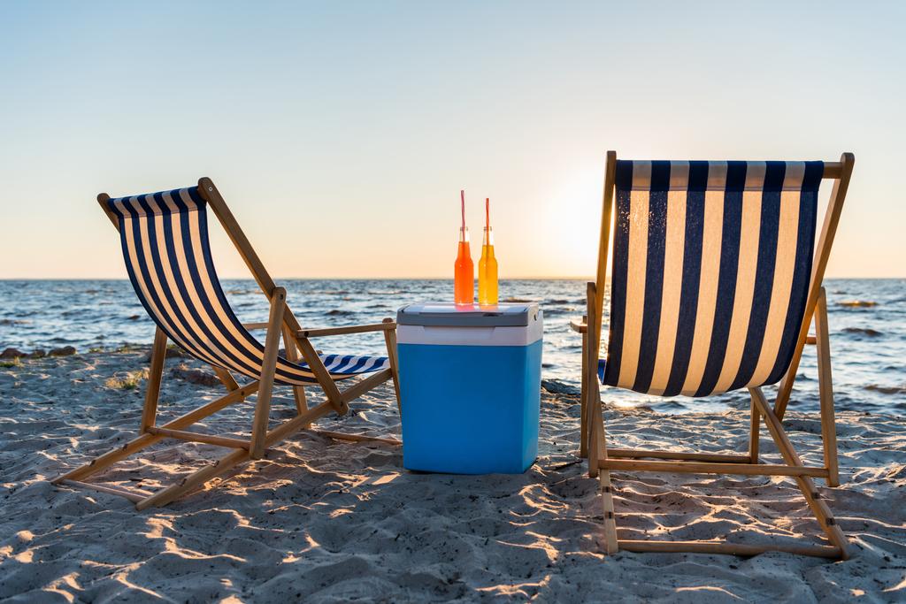 δροσιστικά ποτά στο ψυγείο και ξαπλώστρες στην αμμώδη παραλία στο ηλιοβασίλεμα  - Φωτογραφία, εικόνα