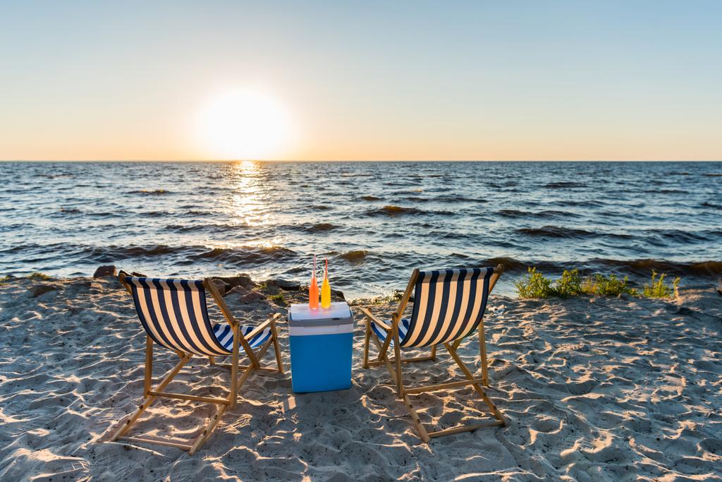 летние напитки на кулере и шезлонгах на песчаном пляже на закате
  - Фото, изображение