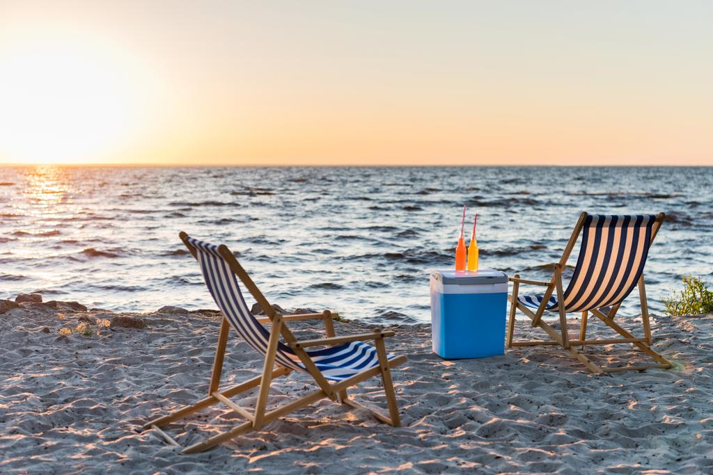 zomer dranken op koeler en chaise lounges op zanderige strand bij zonsondergang  - Foto, afbeelding