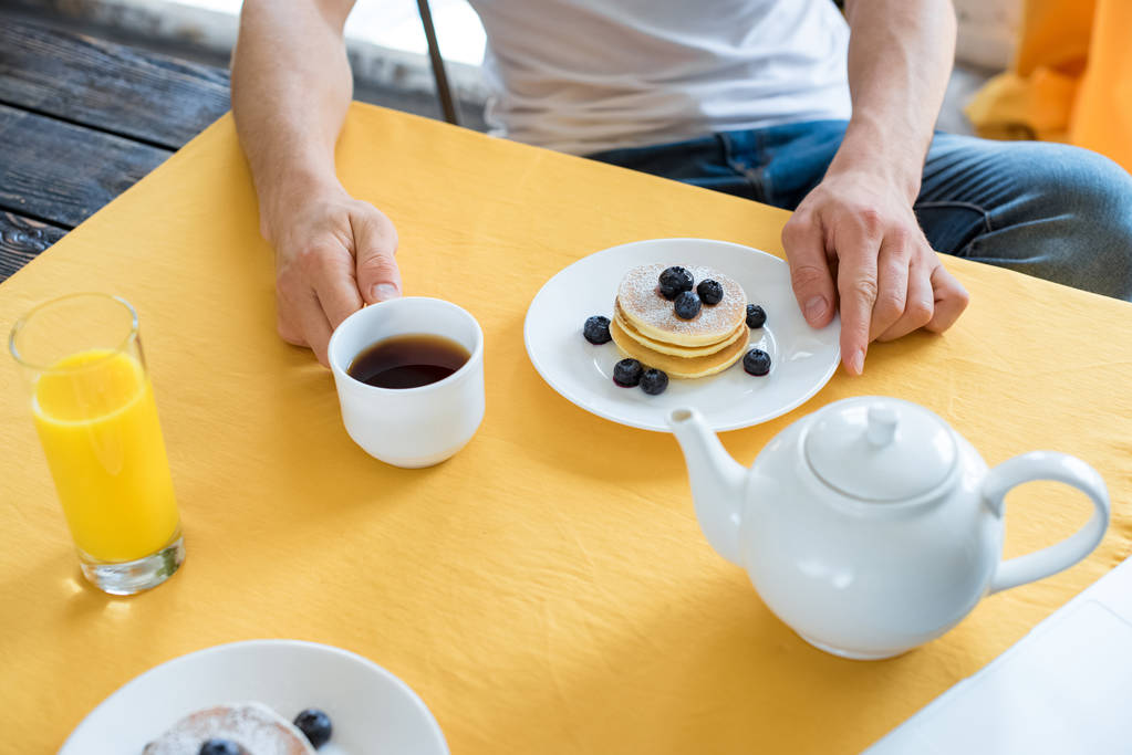 vista parcial do homem sentado à mesa com café da manhã em casa
 - Foto, Imagem