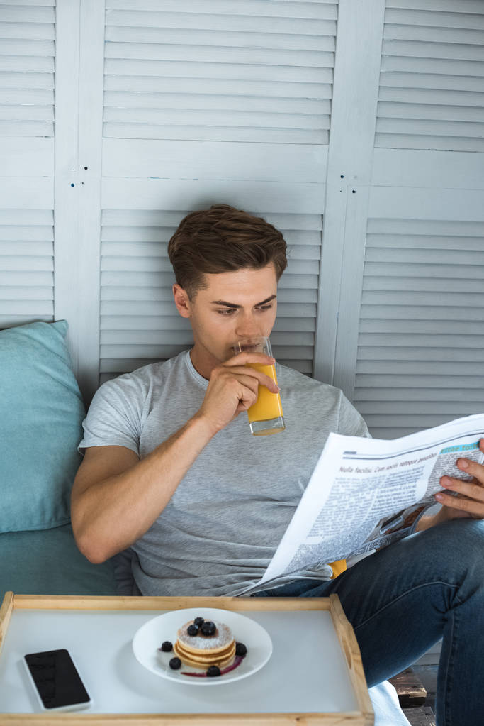 Genç adam sabah yatakta gazete okurken suyu içme portresi - Fotoğraf, Görsel