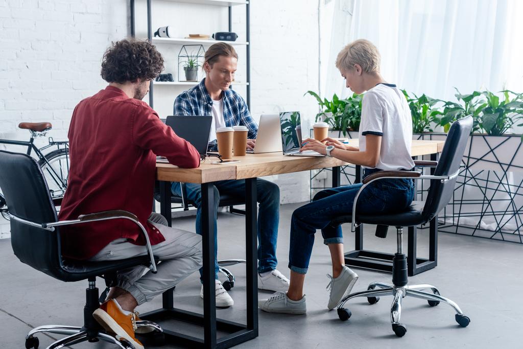 equipe de inicialização jovem usando laptops enquanto sentados juntos no local de trabalho
  - Foto, Imagem