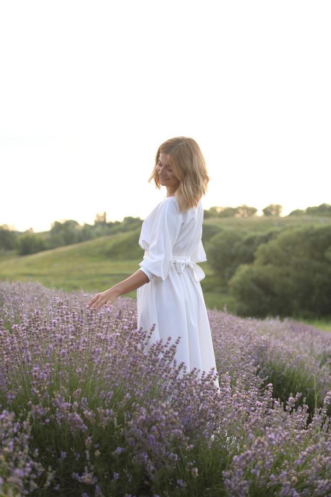attraktive Frau in weißem Kleid, die in violettem Lavendelfeld wandelt und Blumen berührt - Foto, Bild