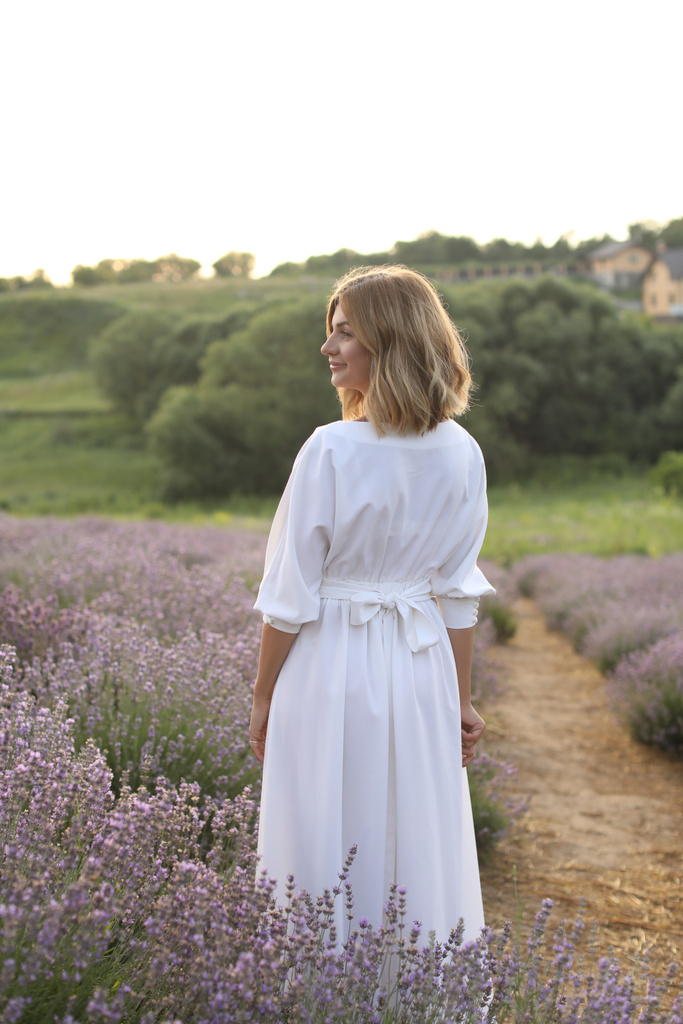 vista posterior de la atractiva mujer en vestido blanco de pie en el campo de lavanda violeta
  - Foto, Imagen