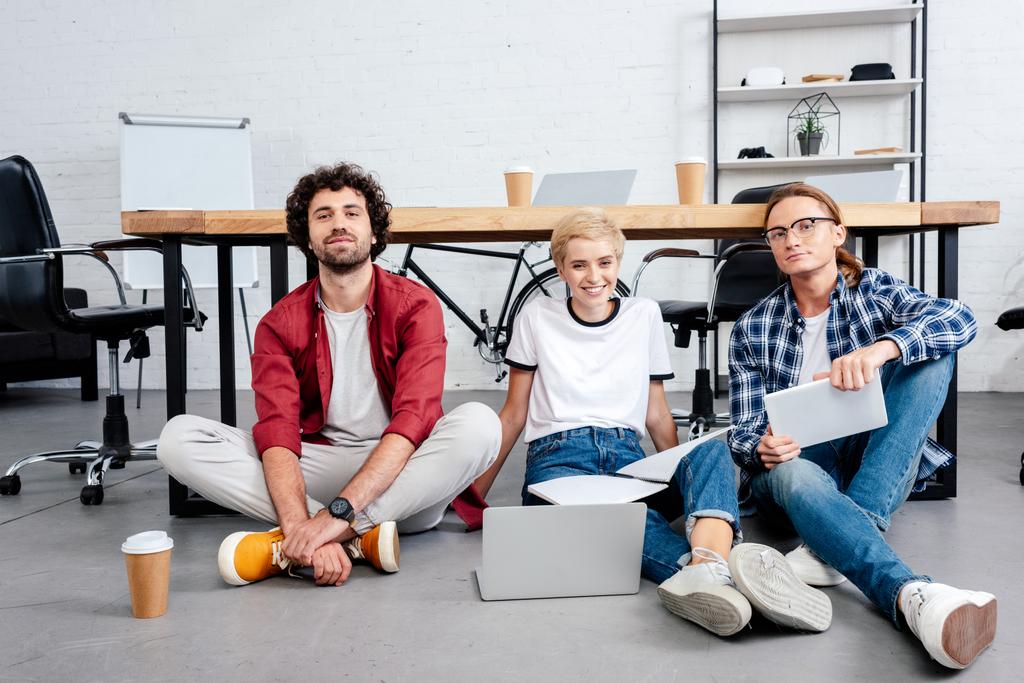 улыбающаяся молодая команда стартапов, сидящая на полу и работающая вместе
 - Фото, изображение
