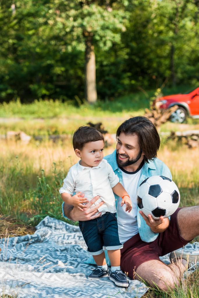 Šťastný otec a batole syn hraje s míčem fotbal na pikniku - Fotografie, Obrázek