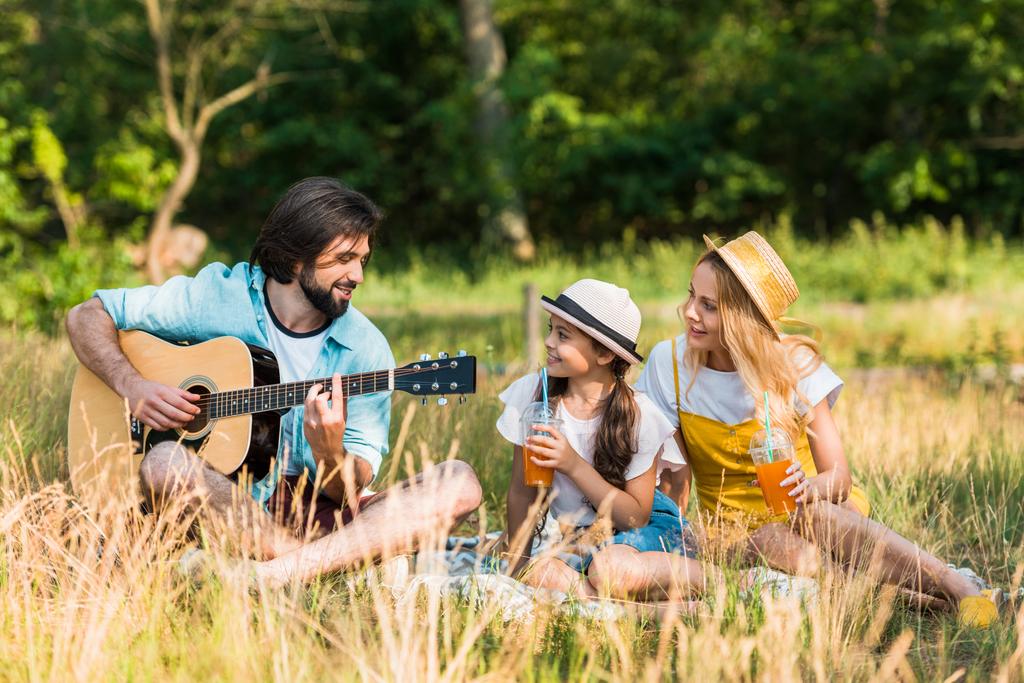glücklicher Vater spielt Akustikgitarre für Tochter und Frau beim Picknick - Foto, Bild