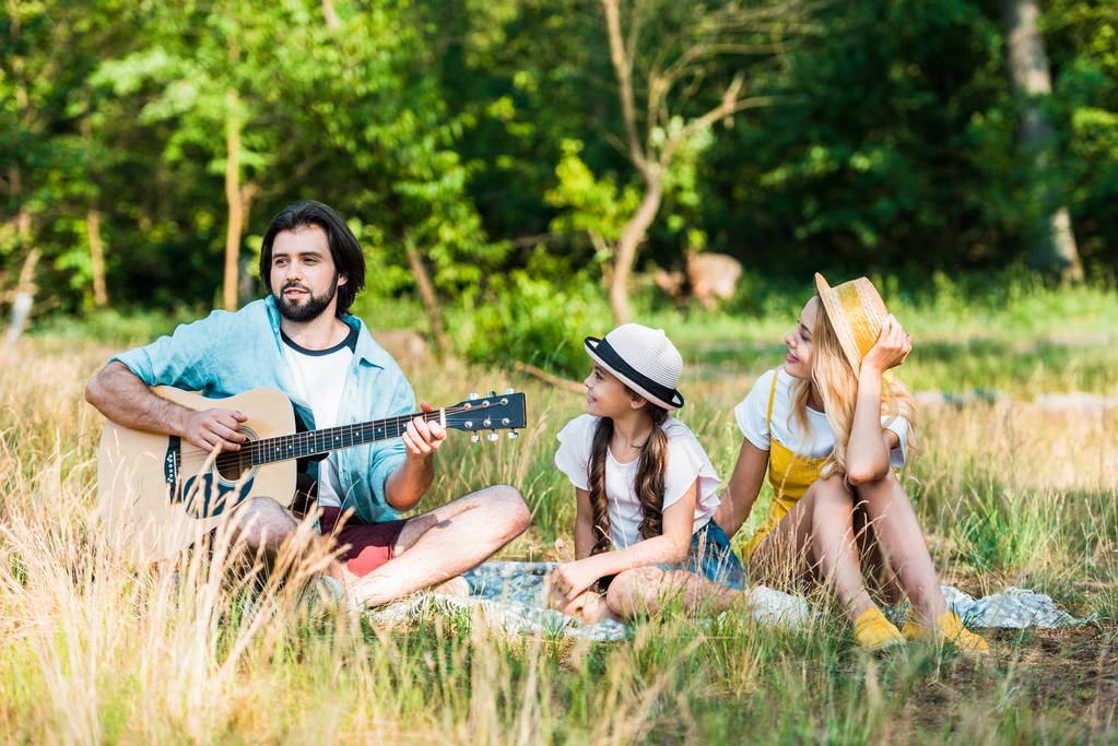 отец играет на акустической гитаре для дочери и жены на пикнике
 - Фото, изображение