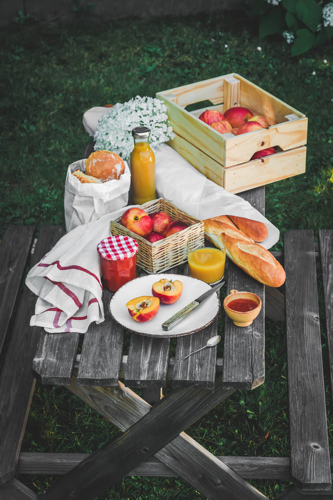 Piknik a fából készült asztal élelmiszerek széles választékát. Lemez, kajszibarack, kis lekváros jar, sokféle kenyér, gyümölcslé glace. Hangulatos nyári reggelit. Nézd meg felülről - Fotó, kép
