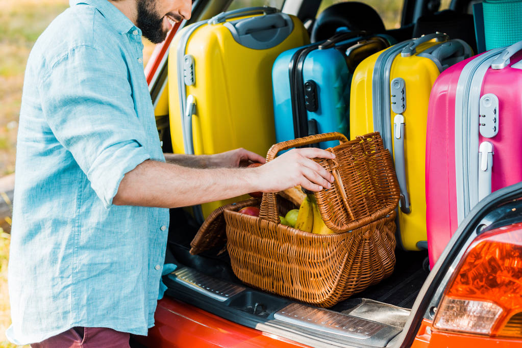 imagen recortada de hombre embalaje cesta de picnic en el maletero del coche
 - Foto, Imagen