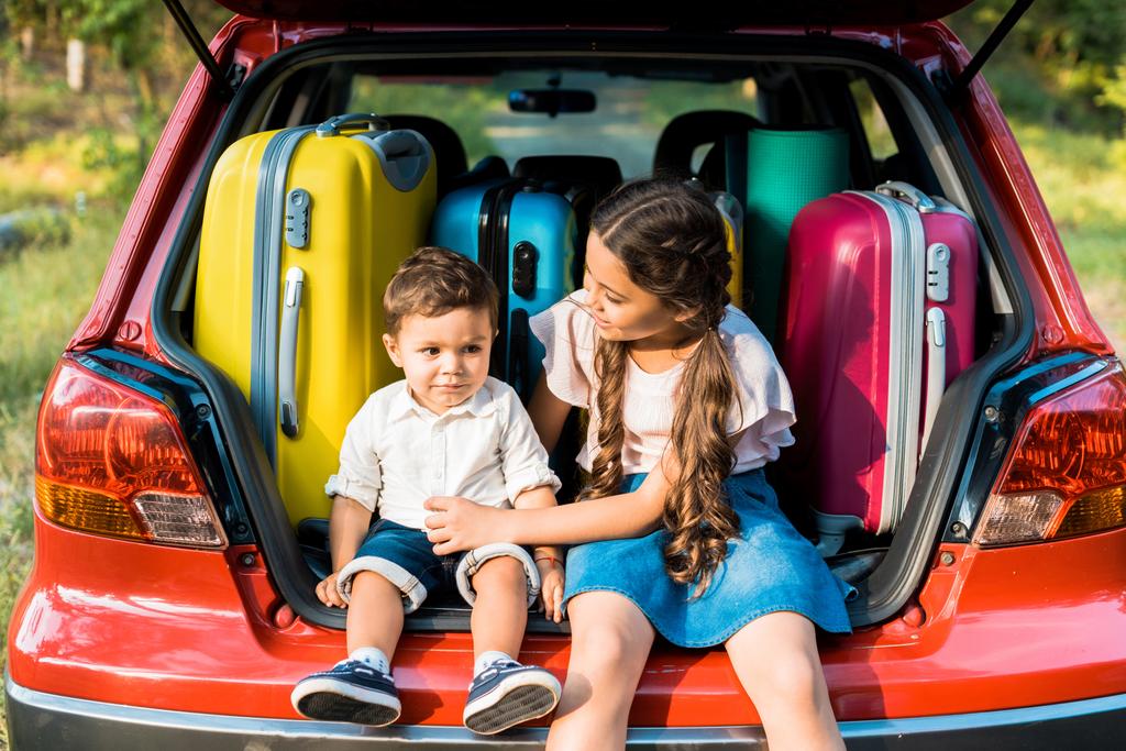 adorable frère et soeur assis près des sacs de voyage dans le coffre de la voiture
 - Photo, image