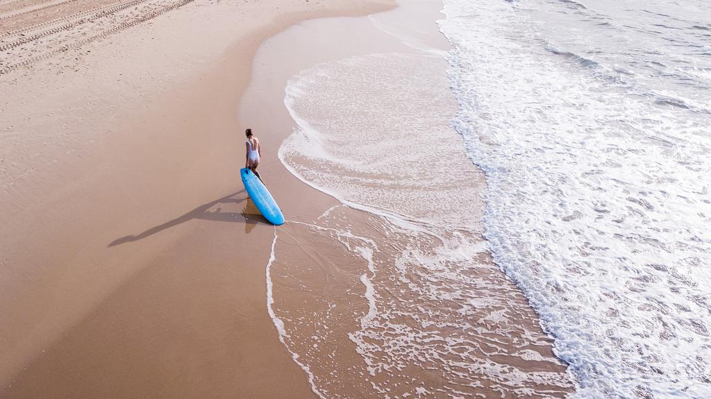 вид с воздуха на молодую женщину в купальнике, тянущую доску для серфинга на песчаном пляже, Ашдод, Израиль
 - Фото, изображение