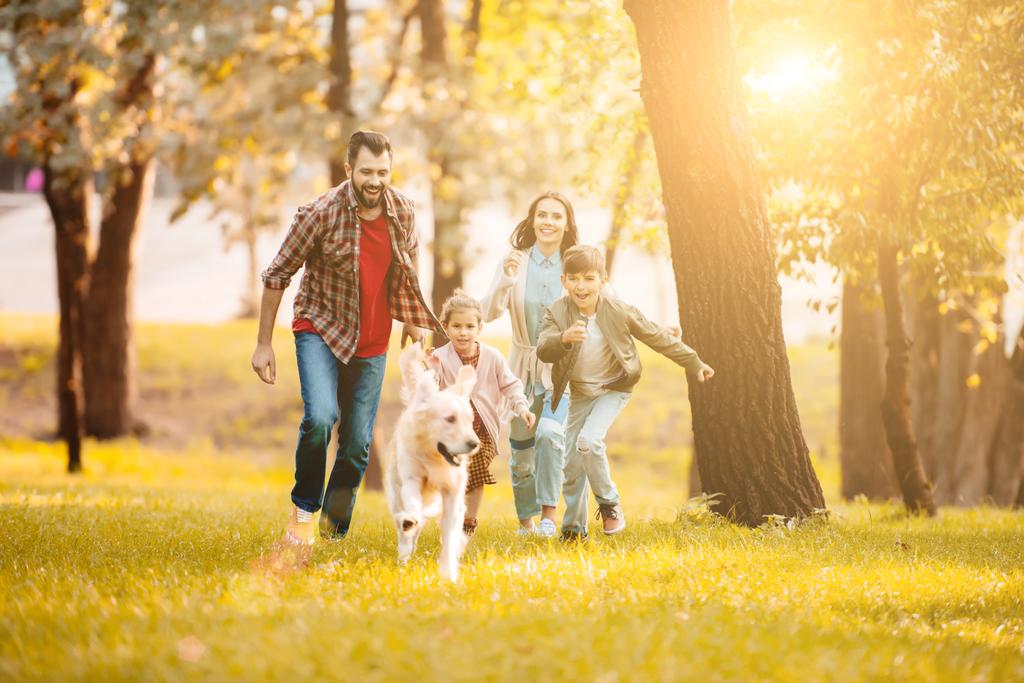 Vorderansicht von lächelndem Paar und Kindern, die mit Golden Retriever im Park rennen  - Foto, Bild