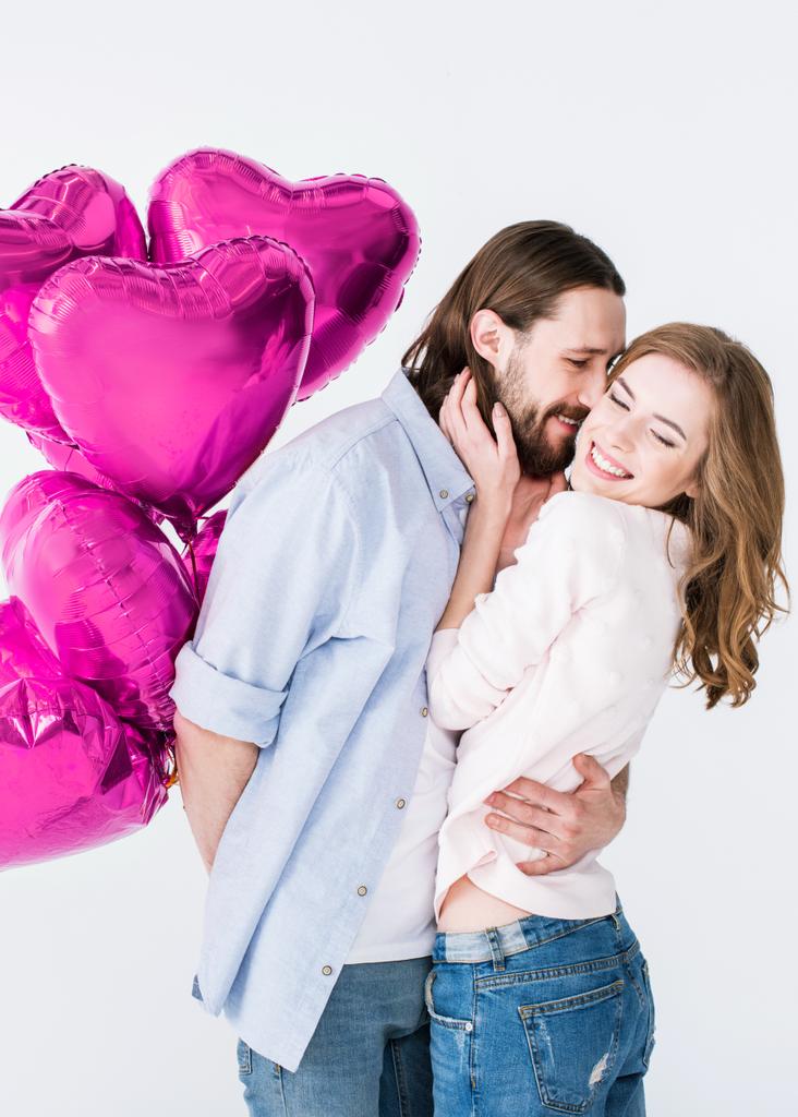 joven guapo sosteniendo globos en forma de corazón y abrazando novia aislada en blanco
  - Foto, imagen
