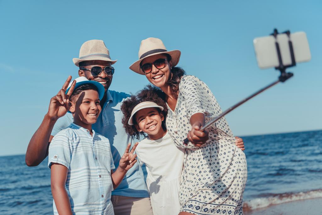 晴れた日のビーチでスマート フォンで若い幸せなアフリカ系アメリカ人家族撮影 selfie - 写真・画像
