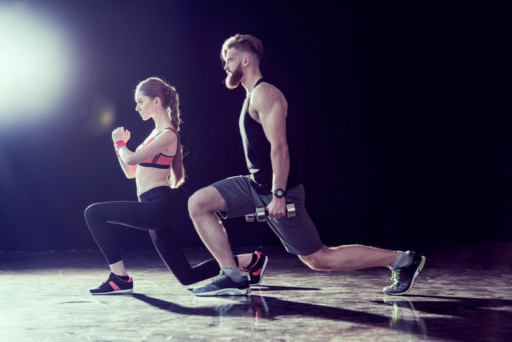 Vista lateral del deportista guapo y la mujer en forma joven entrenando juntos en negro
 - Foto, imagen