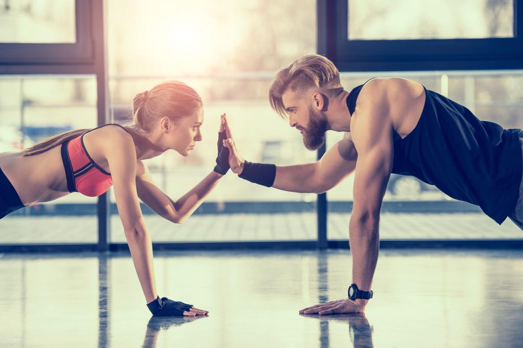 side view of young sportsman and woman doing plank exercise and giving high five - Photo, Image