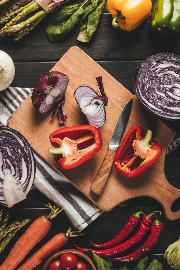Draufsicht auf Schneidebrett mit Messer und verschiedenen frischen Gemüsesorten auf Holztischplatte - Foto, Bild