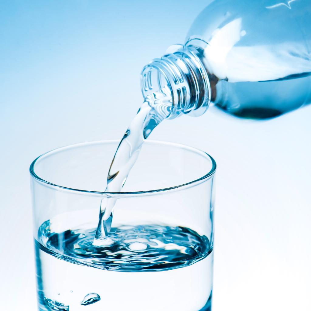 Close-up shot van stromende water uit plastic fles in glas, afgezwakt in blauw - Foto, afbeelding