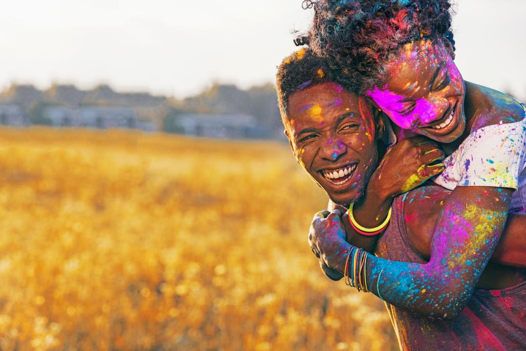 riéndose africano americano pareja piggybacking en holi festival en trigo campo
 - Foto, imagen