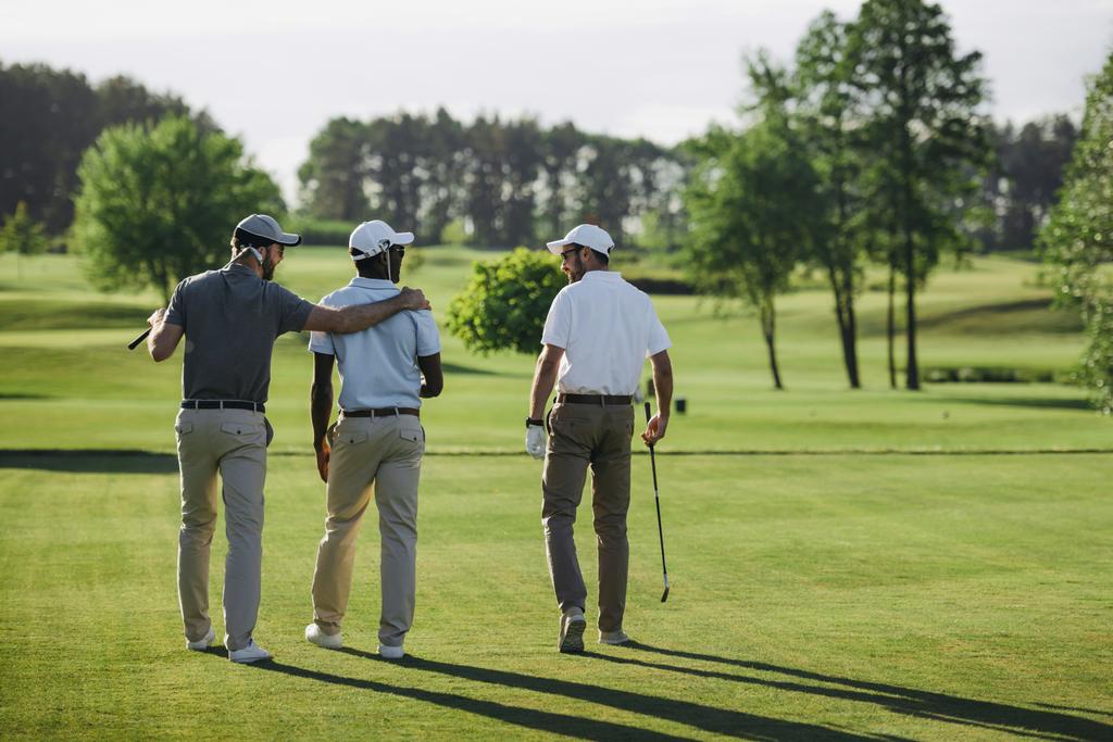 вид сзади мультиэтнических игроков в гольф, идущих по площадке для гольфа
 - Фото, изображение