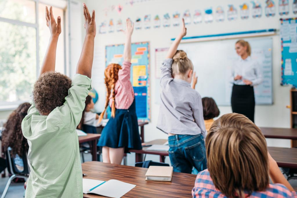 grupo de crianças levantando as mãos em sala de aula para responder a pergunta professores
 - Foto, Imagem