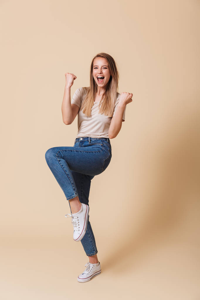 Ολόσωμο πορτρέτο ενός ενθουσιασμένος casual κορίτσι γιορτάζει την επιτυχία με ανοιχτό το στόμα απομονωμένη μπεζ φόντο - Φωτογραφία, εικόνα