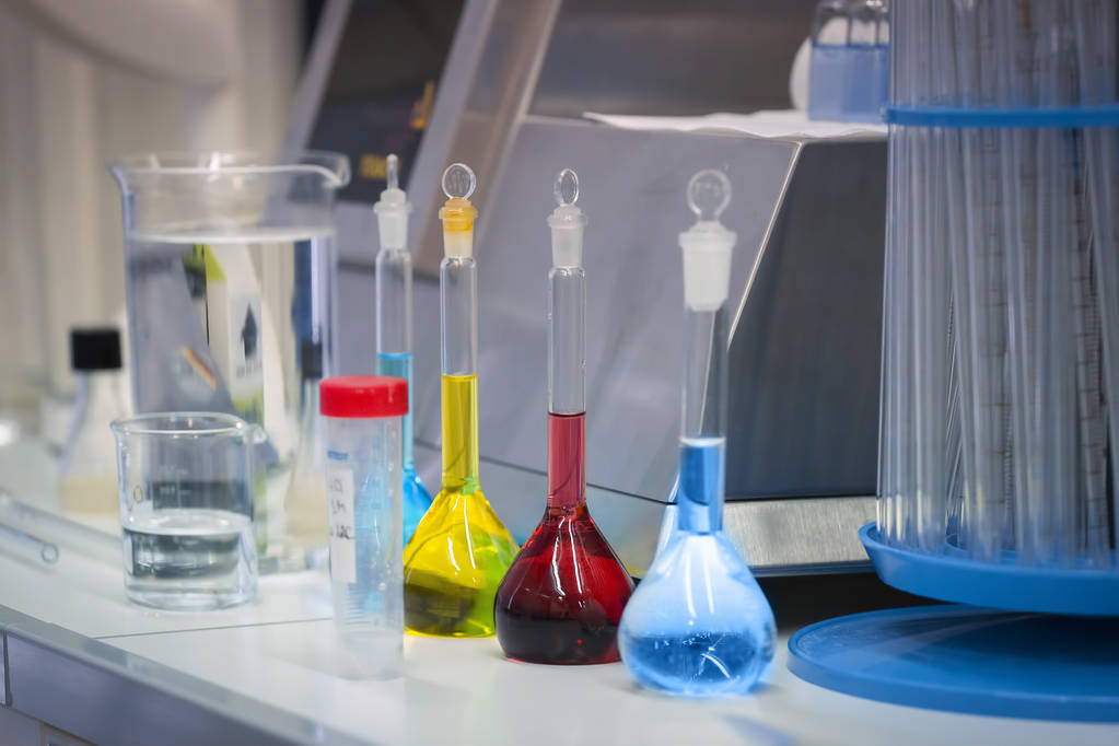 Värikkäissä pulloissa olevat reagenssit ovat pöydällä laboratoriossa
 - Valokuva, kuva