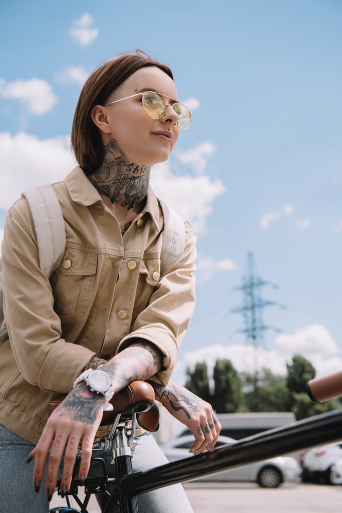 ローアングル街で自転車と一緒に立っているスタイリッシュな刺青女性観  - 写真・画像