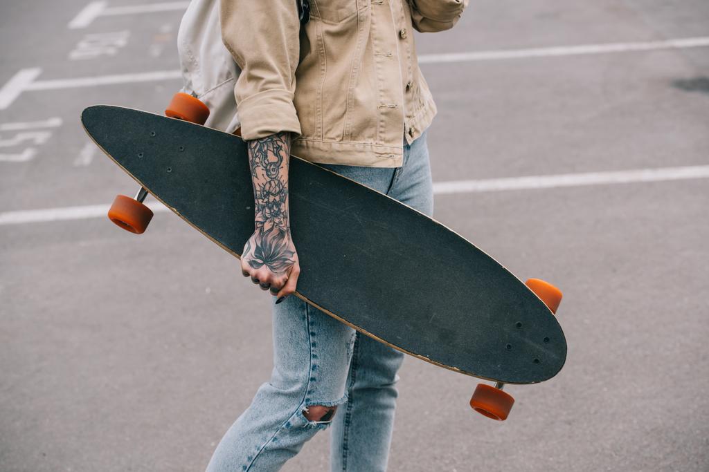  částečný pohled stylové Tetovaný žena držící longboard na parkovišti  - Fotografie, Obrázek
