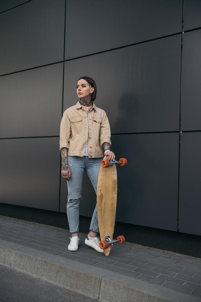 mladá Tetovaný žena stojící s skateboard černé zdi  - Fotografie, Obrázek