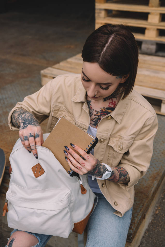 vue grand angle de femme tatouée élégante mettant le manuel dans le sac à dos
  - Photo, image