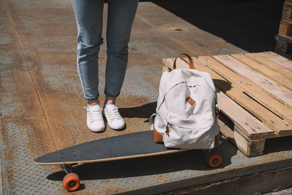 обрезанное изображение женщины, стоящей возле рюкзака и скейтборда
  - Фото, изображение