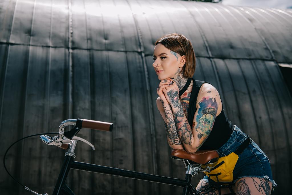 uśmiechający się stylowe tatuażem dziewczyna stojąc z roweru na ulicy - Zdjęcie, obraz
