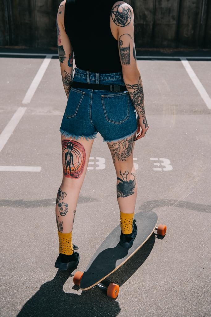 bijgesneden afbeelding van stijlvolle getatoeëerd meisje skateboarden op parkeerplaats  - Foto, afbeelding