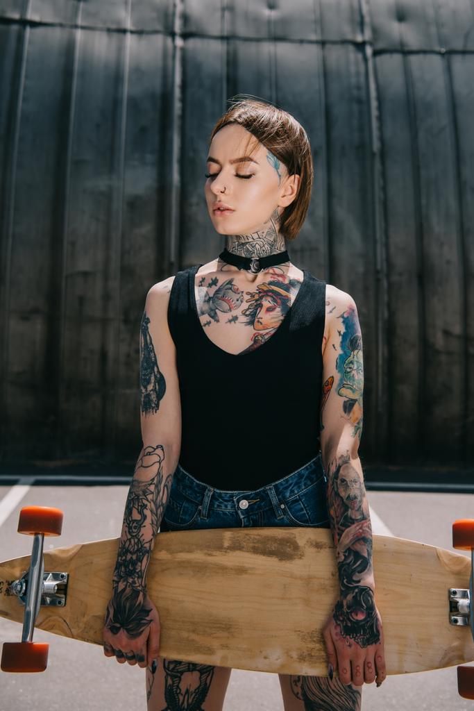 attraente elegante ragazza tatuata con gli occhi chiusi in possesso di skateboard
  - Foto, immagini