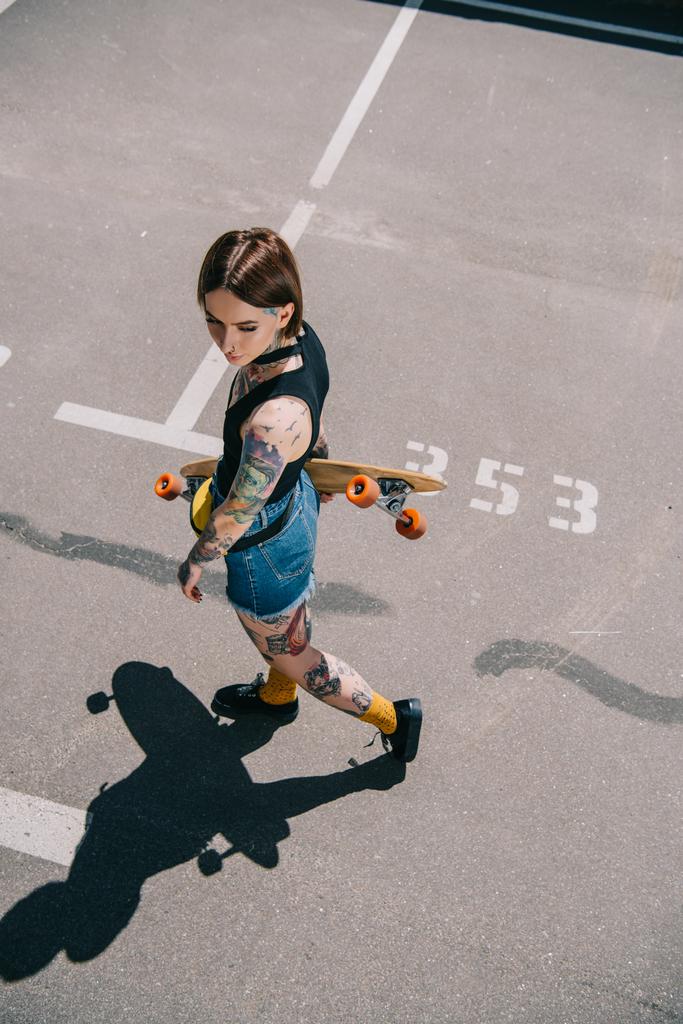 overhead view of young tattooed woman holding skateboard at parking lot  - Photo, Image