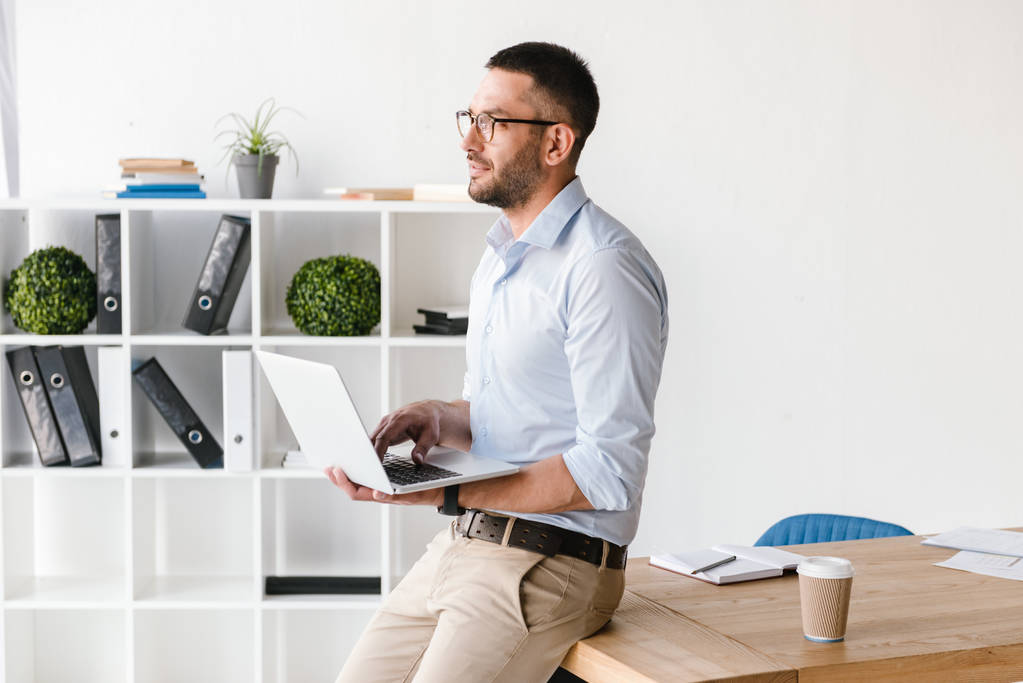 Profiili kuva liikemiehen yllään valkoinen paita istuu pöydällä toimistossa ja katselee eteenpäin, kun käytät hopea laptop töihin
 - Valokuva, kuva