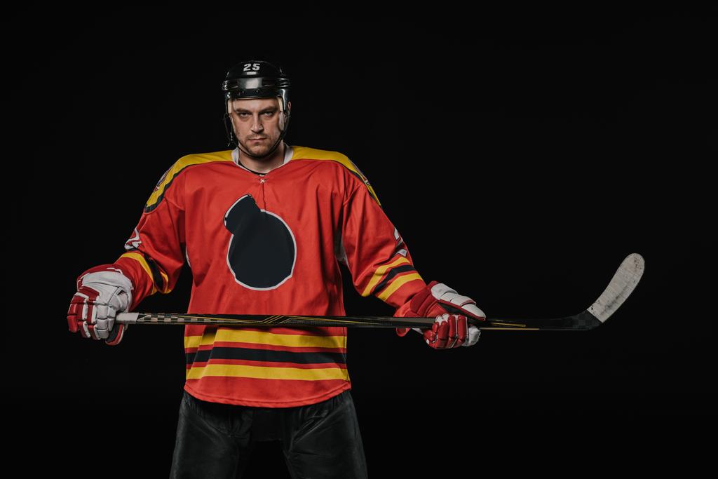 professional ice hockey player holding hockey stick and looking at camera isolated on black - Photo, Image